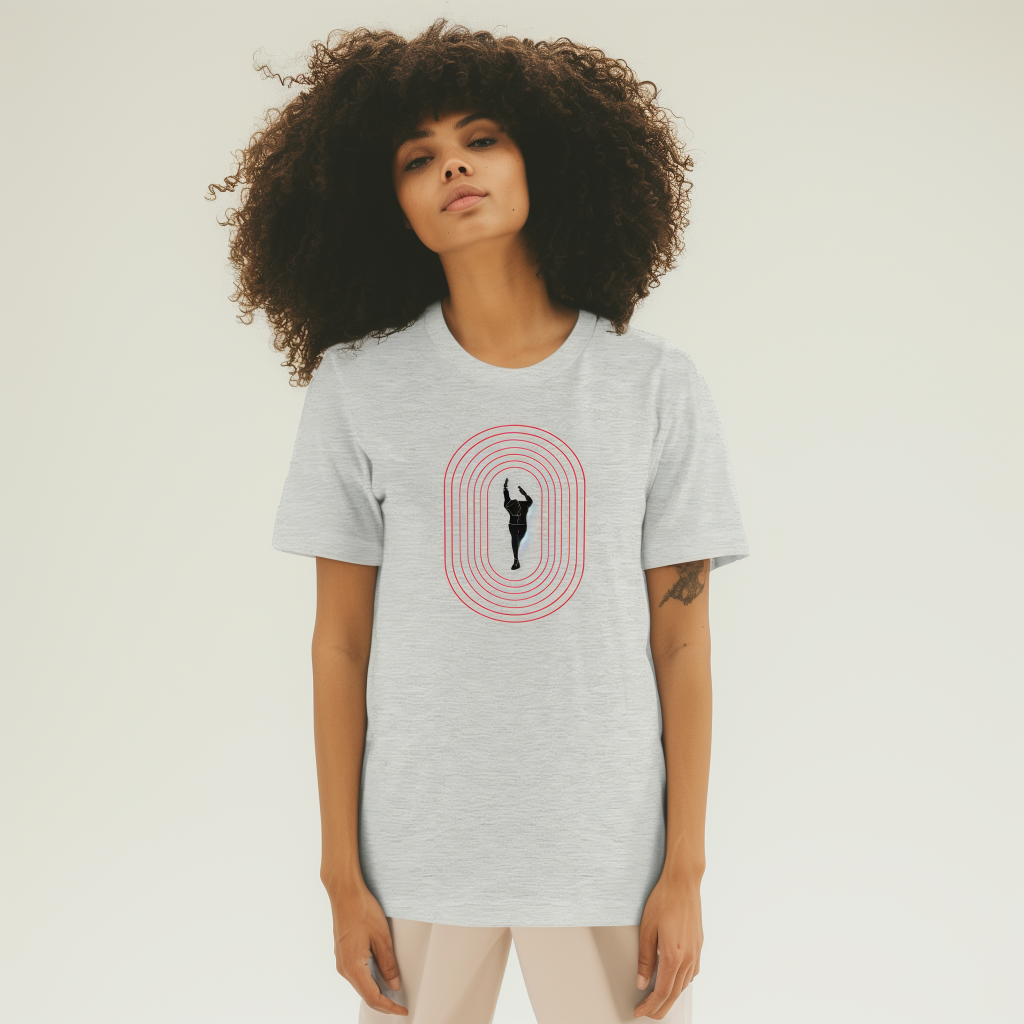 Woman with large curly hair standing against a pale background, wearing a light-gray T-shirt that shows a black silhouette of a person with raised arms inside concentric red oval lines, with a small tattoo visible on her right forearm.