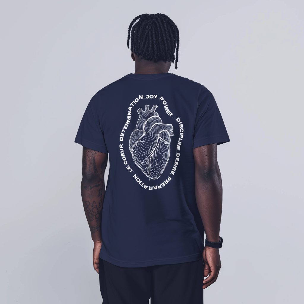 Rear view of a person with short dreadlocks wearing a navy T‑shirt printed with a white anatomical heart illustration surrounded by circular motivational words, showing a tattooed left forearm and a smartwatch on the right wrist against a plain light-gray background.