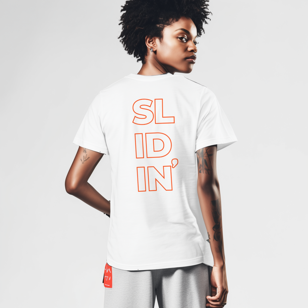 Woman with short textured hair turned back to the camera, looking over her shoulder while wearing a white T-shirt printed vertically in orange-outline letters reading SLIDIN' and gray sweatshorts, with visible arm tattoos against a plain light background.